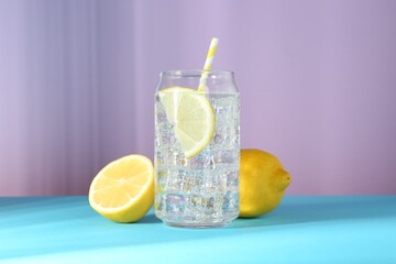 Refreshing lemon water with ice in glass and fresh citrus fruits on color background