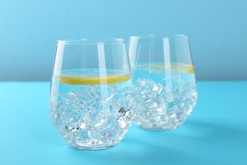 Refreshing water with lemon and ice in glasses on light blue background, closeup
