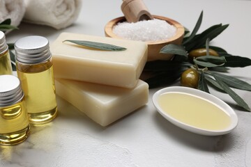 Natural soap bars, olives, oil and sea salt on white marble table, closeup