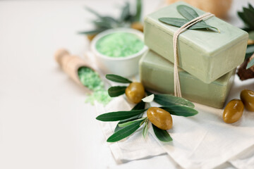 Natural soap bars, olives and sea salt on white table, closeup. Space for text