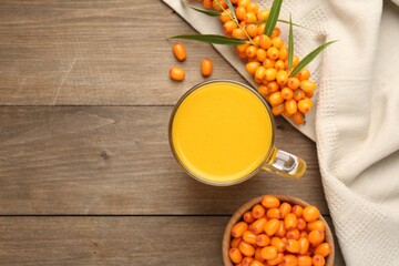 Cup of sea buckthorn tea and fresh berries on wooden table, flat lay. Space for text