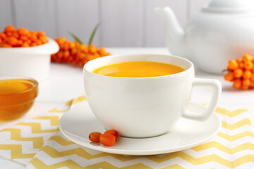 Sea buckthorn tea in cup, honey and fresh berries on white table, closeup