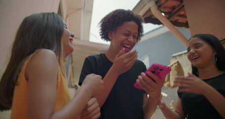 Teenagers laughing and pointing at smartphone screen in suburban alleyway, fun and interactive moment showcasing friendship, digital engagement, and youthful joy
