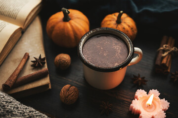 Cozy autumn scene with mug of hot chocolate, book, pumpkins, spices and candles on rustic dark wooden background, warm seasonal atmosphere