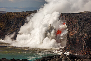 Molten lava flows from a cliff into the ocean, creating a large plume of steam and ash as the hot lava interacts with the cool water.