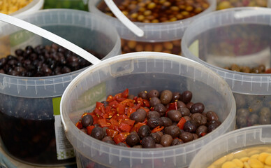 Multiple containers filled with different types of olives and spices are set up at a busy local market
