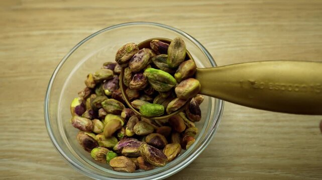 Bowl of unshelled pistachios with a golden scoop on a wooden surface