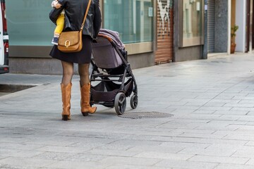 Woman with a baby in her arms and a baby carrier walking down a shopping street. © Manuel