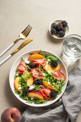 Fresh salad with peaches, arugula, feta, prosciutto and berries in a plate on a light background
