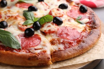 Delicious pizza with cheese, salami, olives and basil on table, closeup