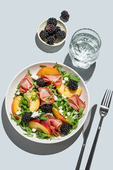Salad with peaches, arugula, feta, prosciutto and berries in a plate on a blue background
