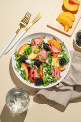 Salad with peaches, arugula, feta, prosciutto and berries in a plate on a yellow background