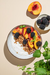 Natural greek yogurt with granola or muesli, peach and blackberry in a bowl on a beige background