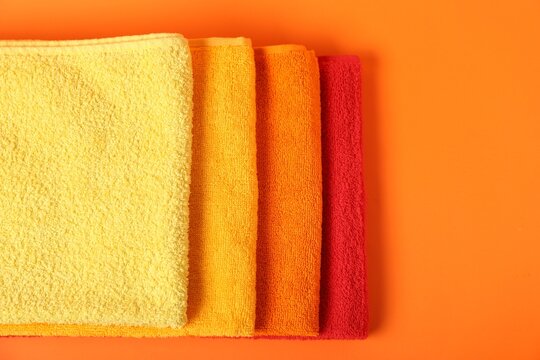 Fresh terry towels on orange background, top view