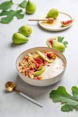 Natural yogurt with granola, figs and honey in a bowl on a light background