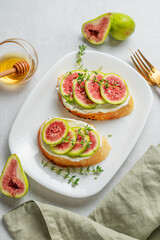 Toasts with fresh figs, cheese, thyme, and honey on a light background.
