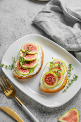 Sweet toasts with fresh figs, cheese, thyme, and honey on a gray background.