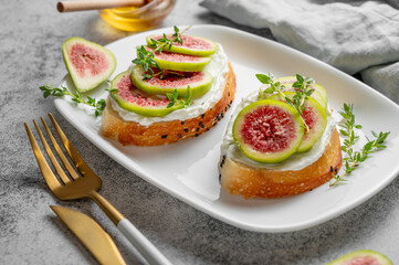 Sweet toasts with fresh figs, cheese, thyme, and honey on a gray background close up.