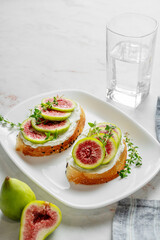 Sweet toasts with fresh figs, cream cheese, thyme, and honey on a marble background.