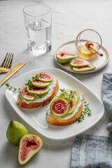 Sweet toasts with fresh figs, cream cheese, thyme, and honey on a marble background.