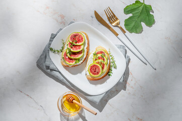 Sweet toasts with fresh figs, cream cheese, thyme, and honey on a marble background.
