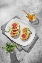 Sweet toasts with fresh figs, cream cheese, thyme, and honey on a gray background.