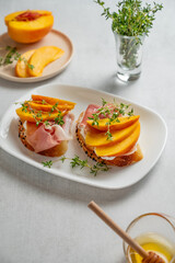 Toast with peach, cream cheese, ham and honey on a plate on a light background