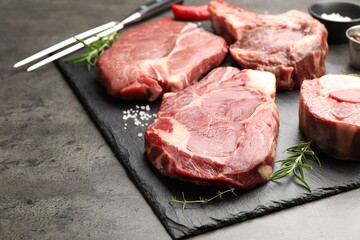 Pieces of raw beef meat, spices and carving fork on grey table, closeup. Space for text