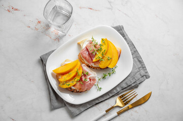 Toast with peach, cream cheese, ham and honey on a plate on a marble background