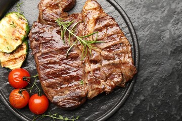 Delicious grilled beef steak with rosemary, zucchini and tomatoes on dark textured table, top view. Space for text
