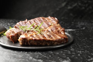 Delicious grilled beef steak with rosemary on dark textured table, closeup