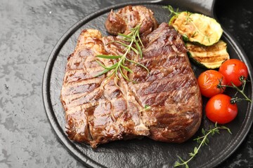 Delicious grilled beef steak with rosemary, zucchini and tomatoes on dark textured table, closeup