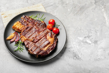 Delicious grilled beef steak with rosemary, onion and tomatoes on grey textured table. Space for text