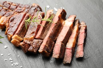 Pieces of delicious grilled beef steak with rosemary and salt on grey textured table, closeup