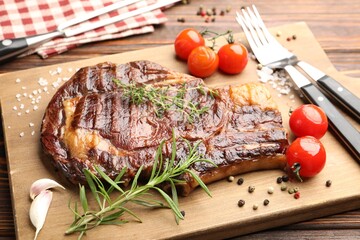 Delicious grilled beef steak with herbs, spices, products and cutlery on wooden table, closeup