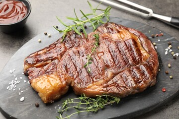 Delicious grilled beef steak with herbs, spices and ketchup on grey textured table, closeup