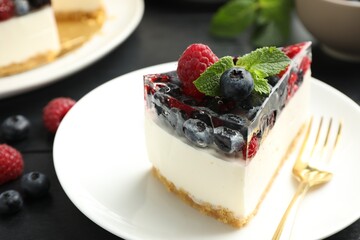 Piece of delicious cheesecake with berries and mint on black wooden table, closeup