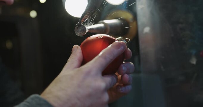A man is engraving a red ornament at Christmas market in Germany.. The ornament is being shaped into a Christmas tree, slow motion