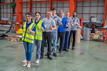 Fototapeta premium Diverse team of engineers and factory workers standing in line inside an industrial warehouse, wearing safety gear and holding helmets, symbolizing teamwork and workplace diversity.
