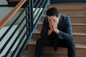 Fototapeta premium Businessman sitting on stairs, experiencing mental health issues or work related stress, feeling despair and exhaustion