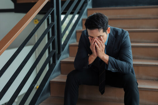 Businessman sitting on stairs, experiencing mental health issues or work related stress, feeling despair and exhaustion