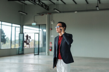 Asian businessman making a phone call, inspecting a large, empty commercial warehouse or office...