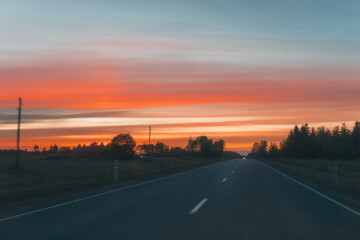 Empty country road leading into horizon under dramatic red and orange sunset sky, scenic evening...