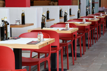 Outdoor restaurant tables with red chairs, olive oil bottles and cutlery neatly arranged