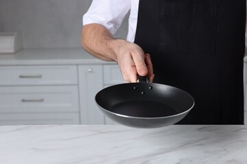 Chef holding frying pan at white marble table in kitchen, closeup. Space for text