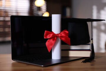 Graduation cap, laptop, books and diploma on wooden table, closeup