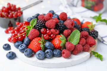 Different ripe berries and mint leaves on white tiled table, closeup