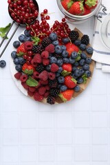 Different ripe berries and mint leaves on white tiled table, flat lay. Space for text