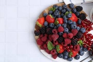 Different ripe berries and mint leaves on white tiled table, top view. Space for text