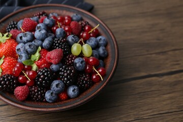 Different ripe berries in bowl on wooden table, closeup. Space for text